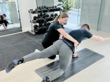An Align Health Collective clinician guiding a patient through a four-point kneeling exercise on a mat.